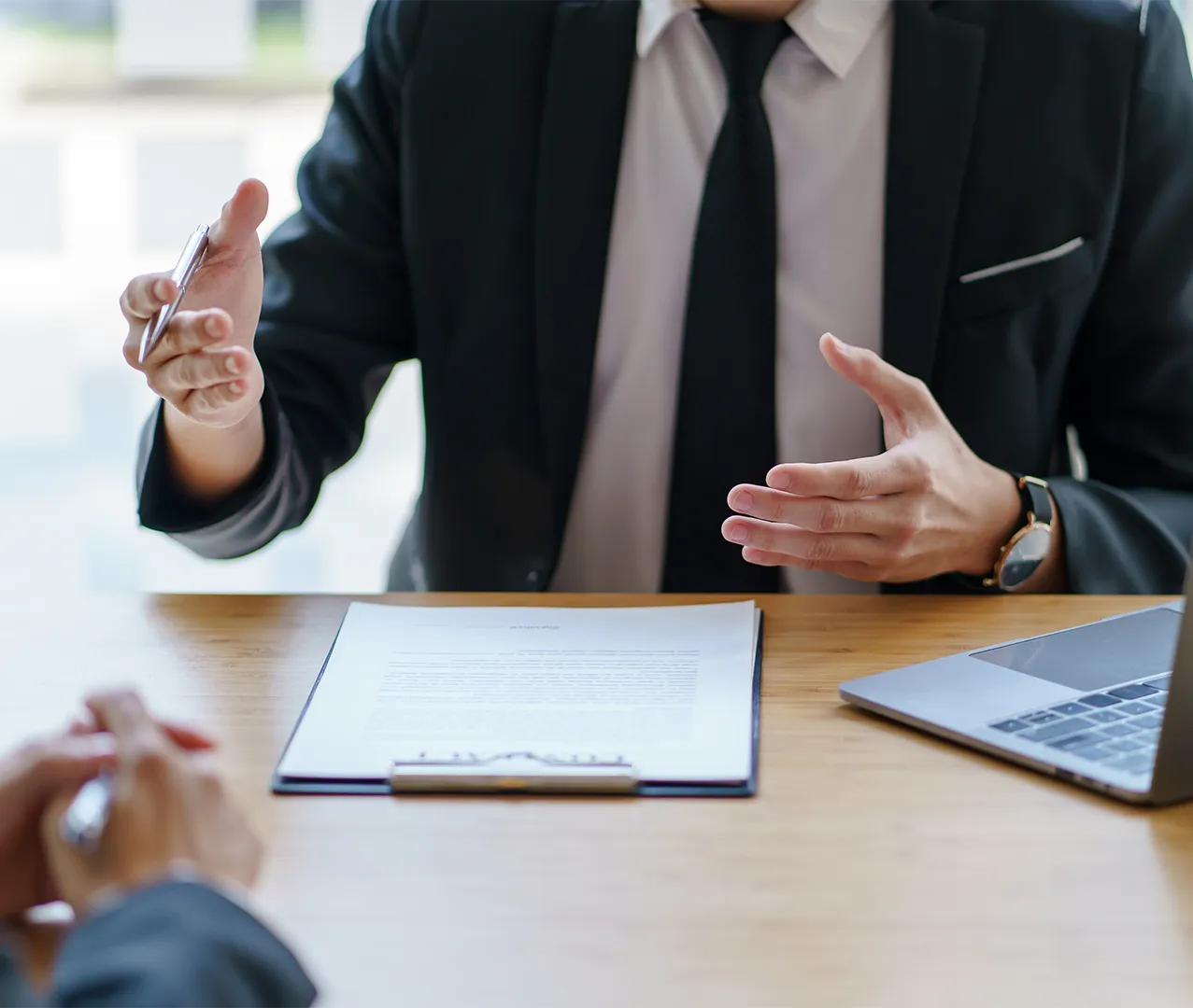 Businessman in suit gesturing during a meeting with documents and laptop on the table.