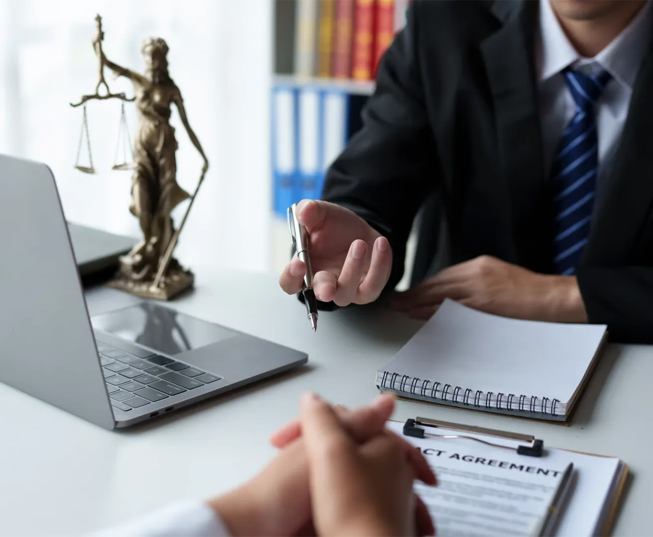 Businessman in suit holding pen over contract with scales of justice and laptop nearby.