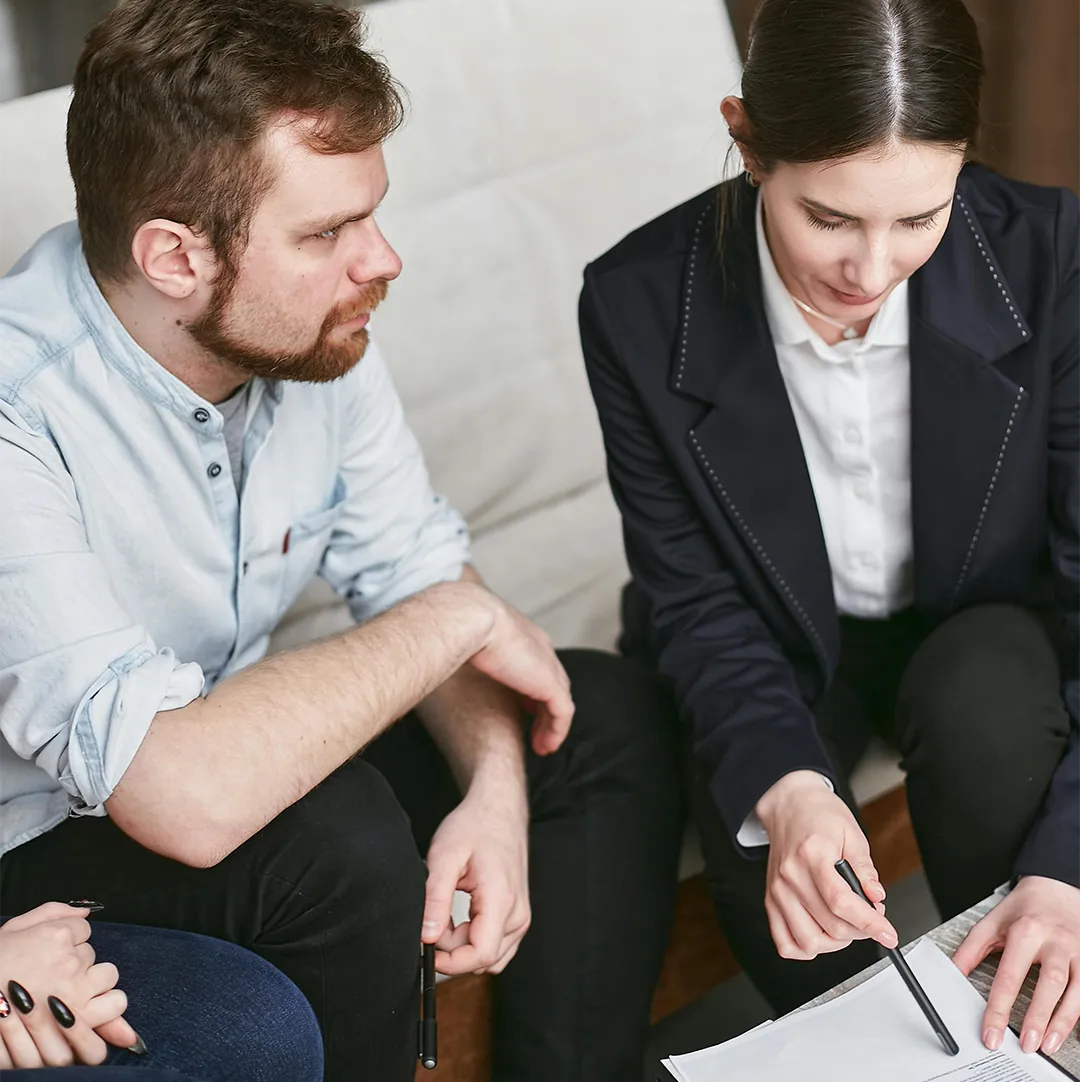 Two people seated discussing and pointing at papers on a low table.