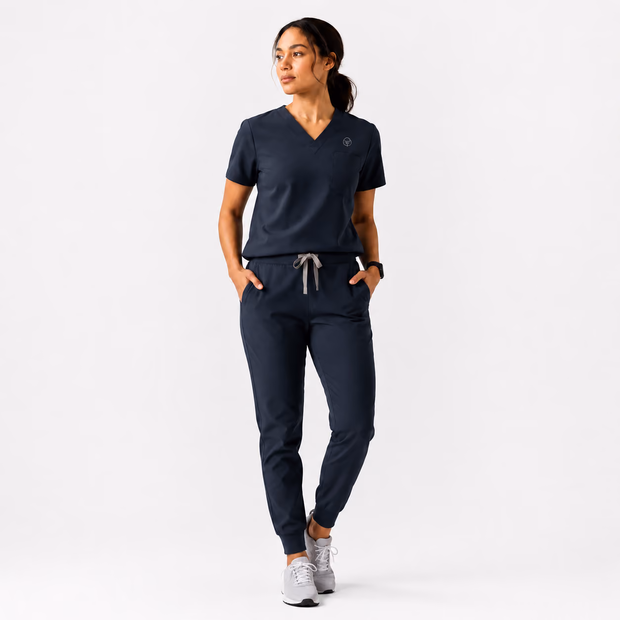 Woman wearing navy scrubs with a v-neck top and drawstring jogger pants, standing against white background.