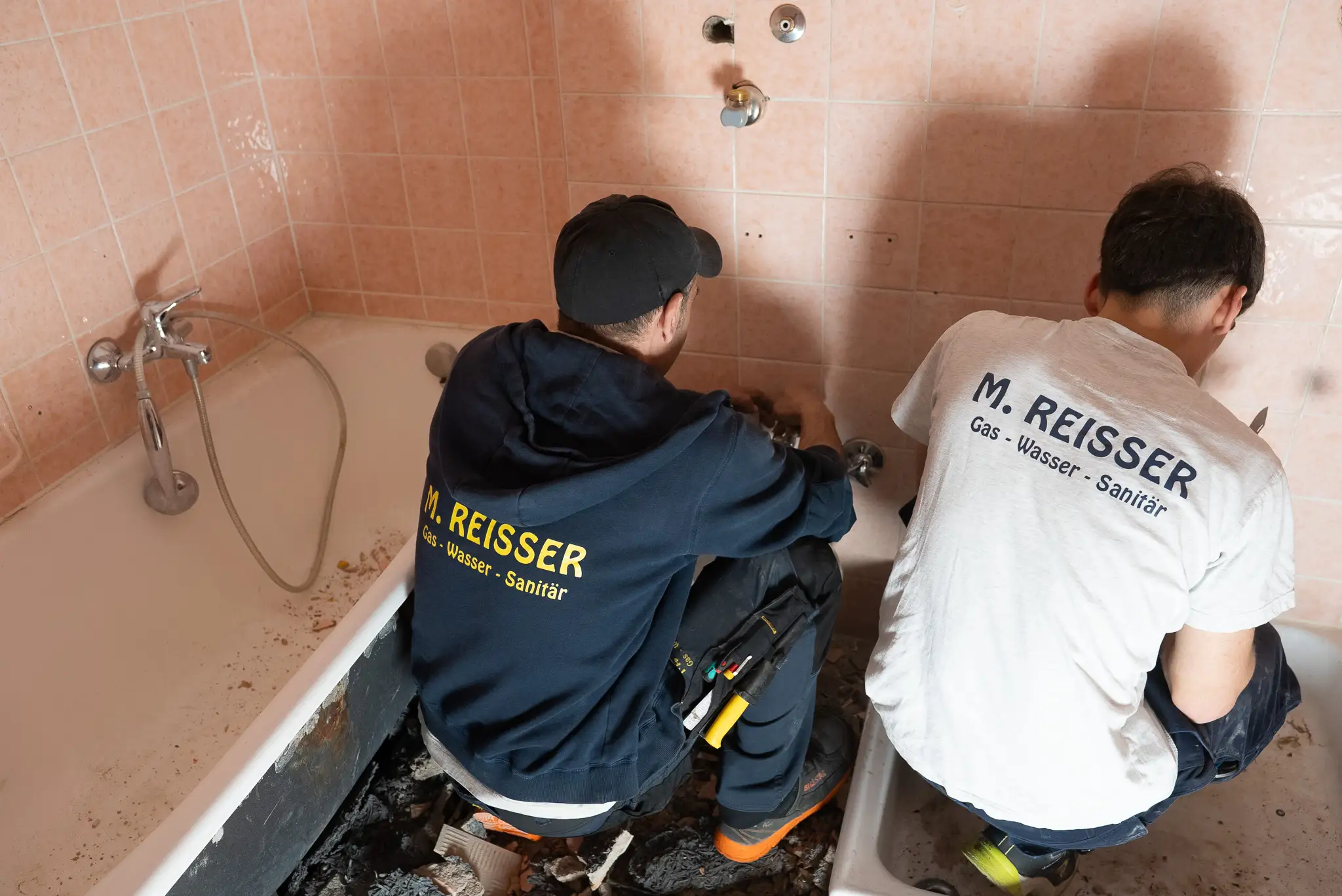 Zwei Handwerker montieren eine große Platte in einem Badezimmer mit Badewanne.
