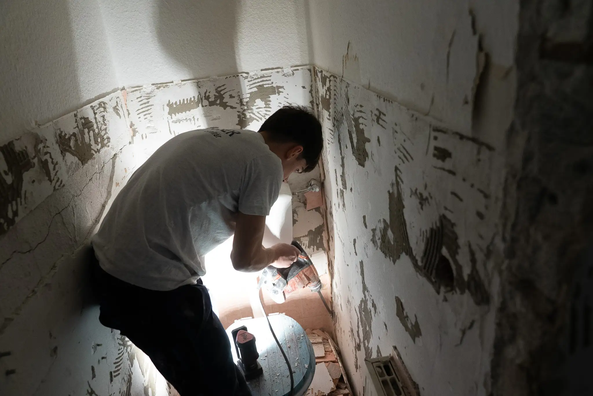 Handwerker entfernt Wandverkleidung mit elektrischem Bohrer in einem alten, teils beschädigten Raum.