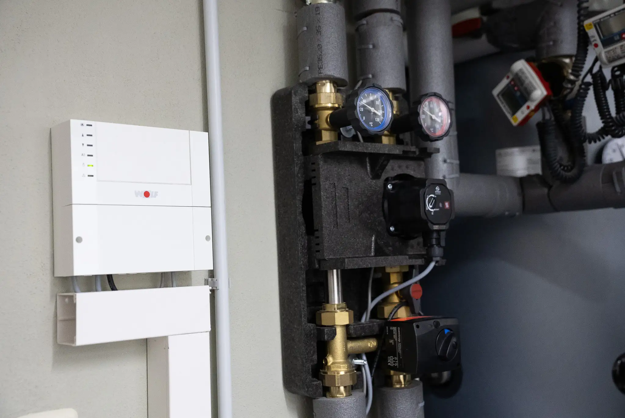 Heizungstechnik mit Druckmessern, Regelventilen, schwarzen Steuergeräten und isolierten Rohren an der Wand.