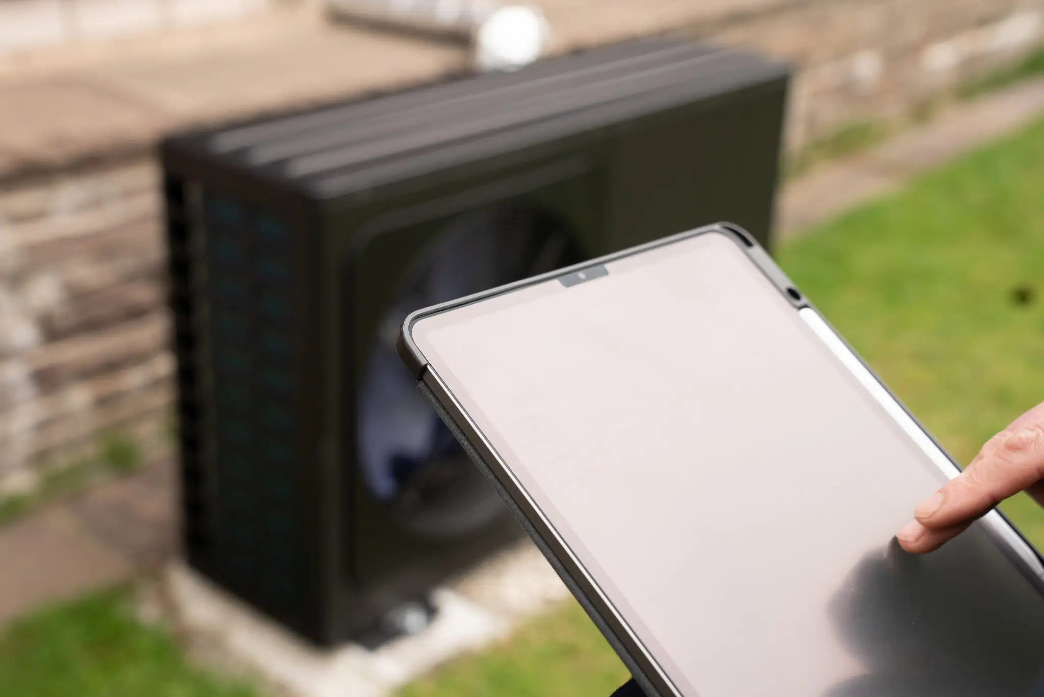 Person bedient Tablet zur Steuerung einer Wärmepumpe im Garten.