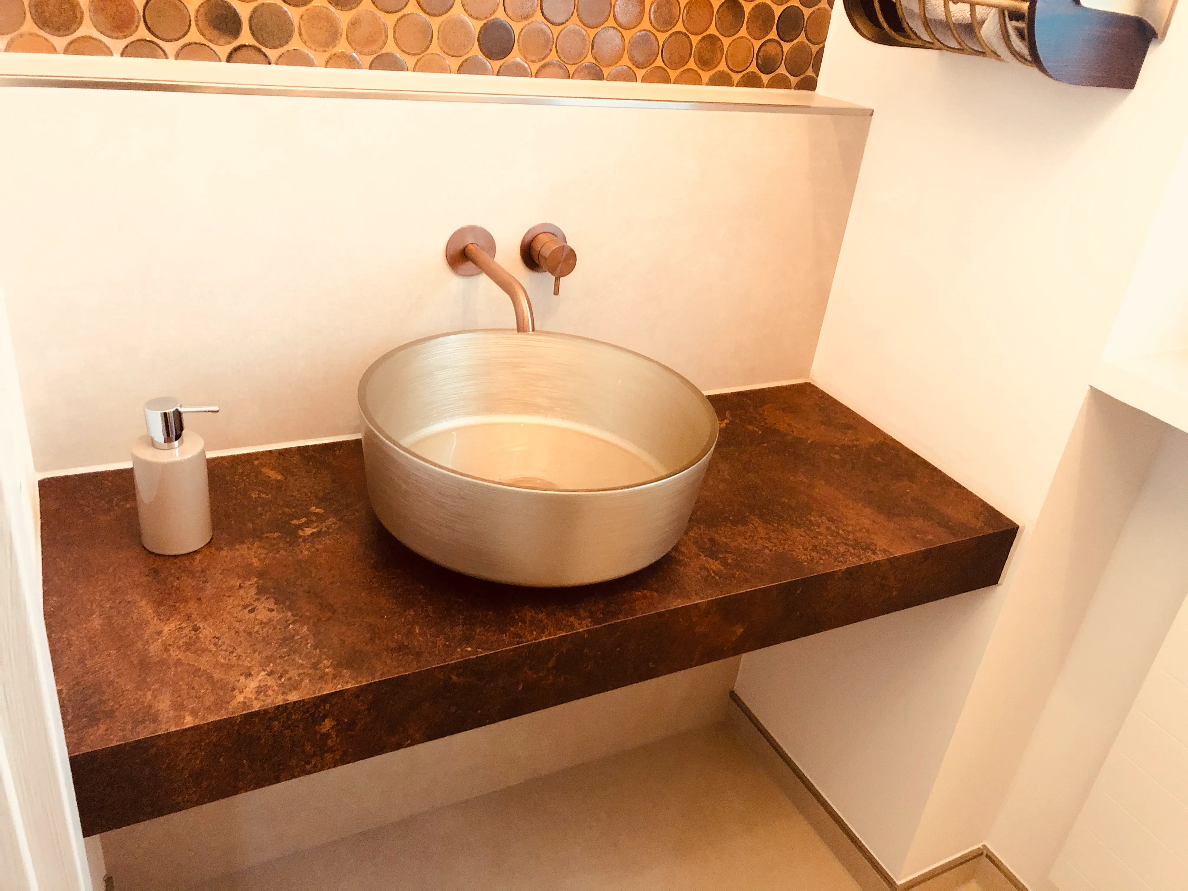 Modern bathroom sink with round beige basin, bronze faucet, soap dispenser on brown countertop.