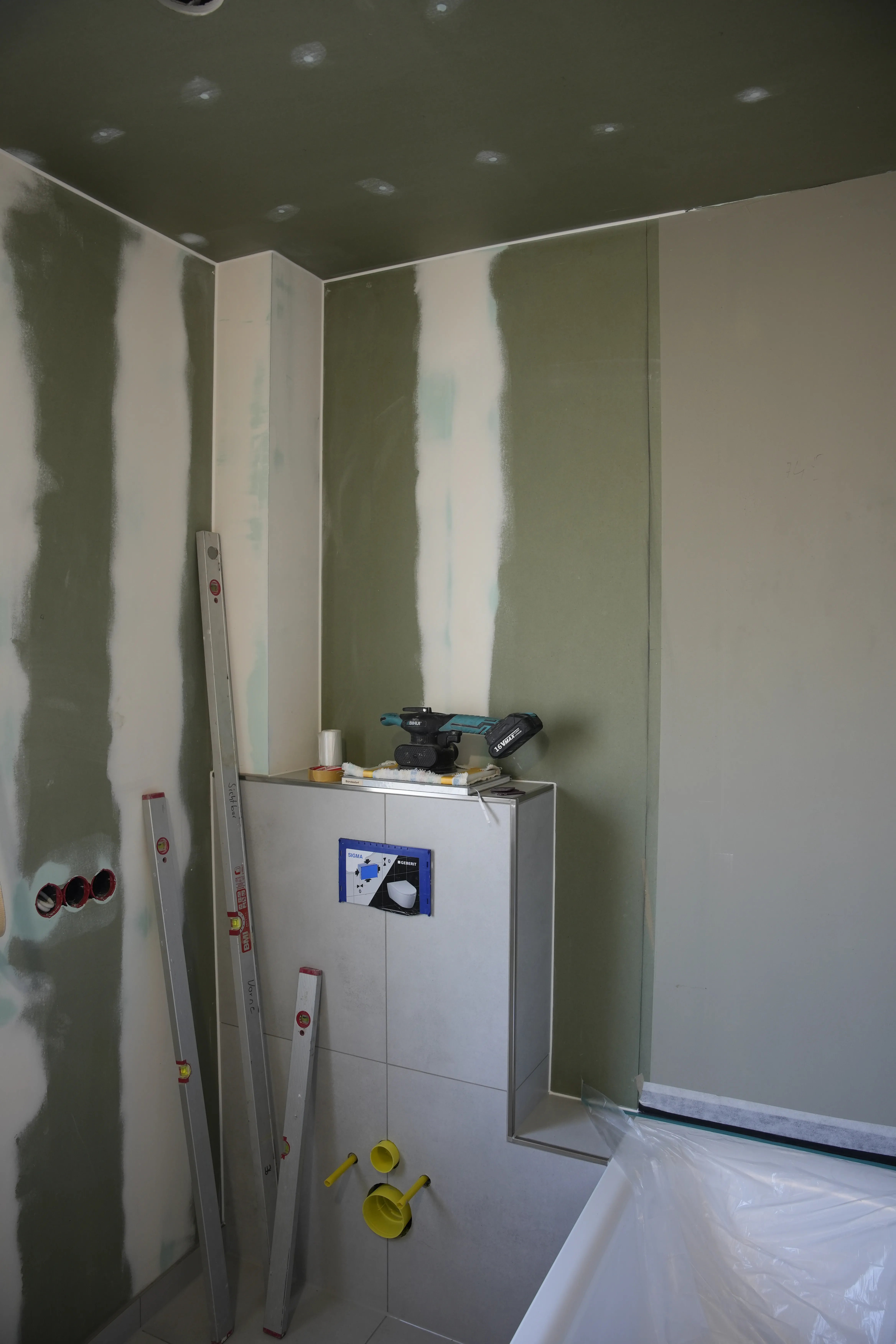 Ein Handwerker glättet Fliesenfugen in einem hellen Badezimmer mit Glättwerkzeug.