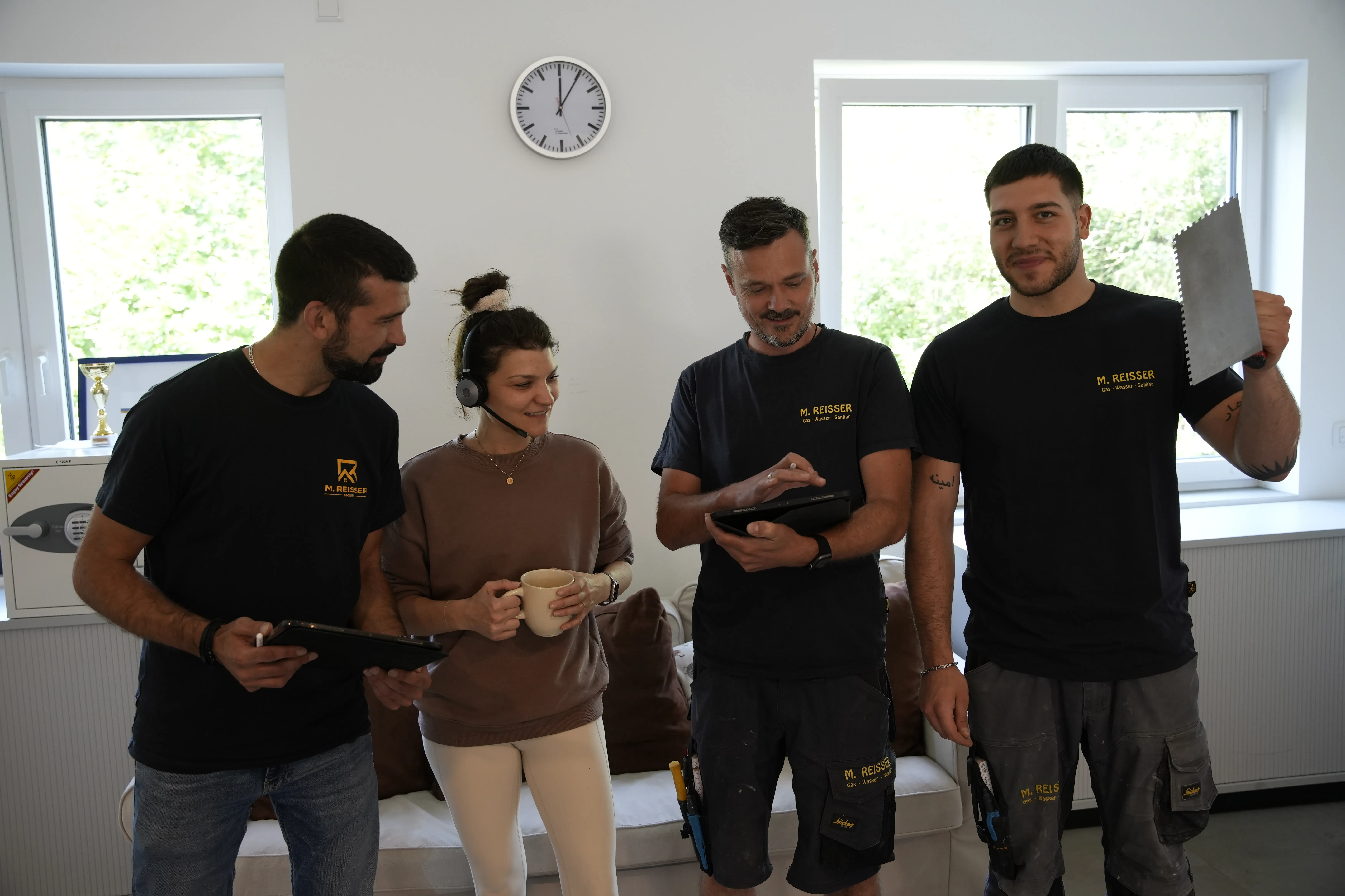 Vier Handwerker und eine Frau in einem hellen Raum, die digital zusammenarbeiten und lächeln.