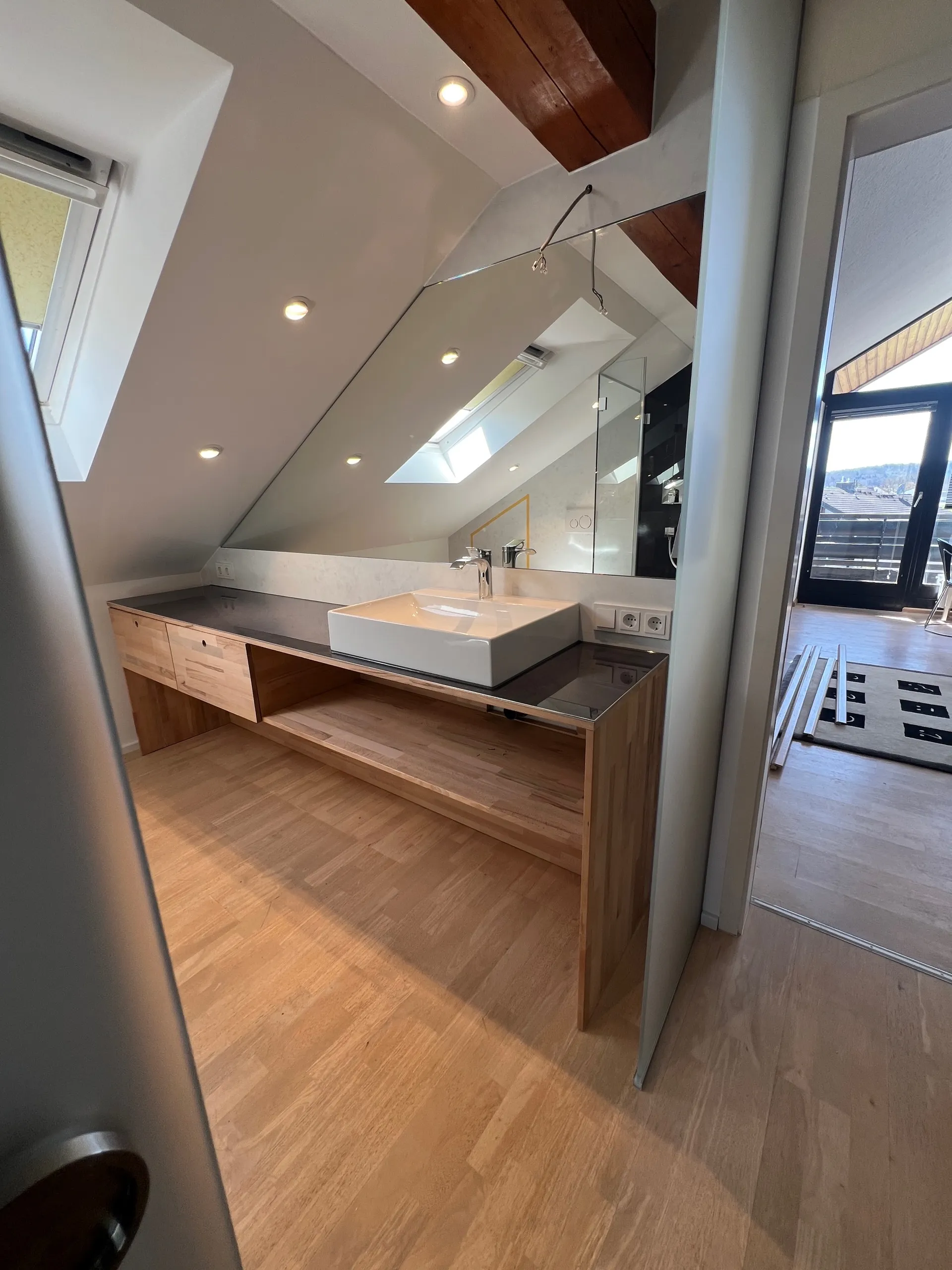 Modernes Badezimmer mit Holzwaschtisch, weißem Waschbecken und großem Spiegel unter Dachschräge.