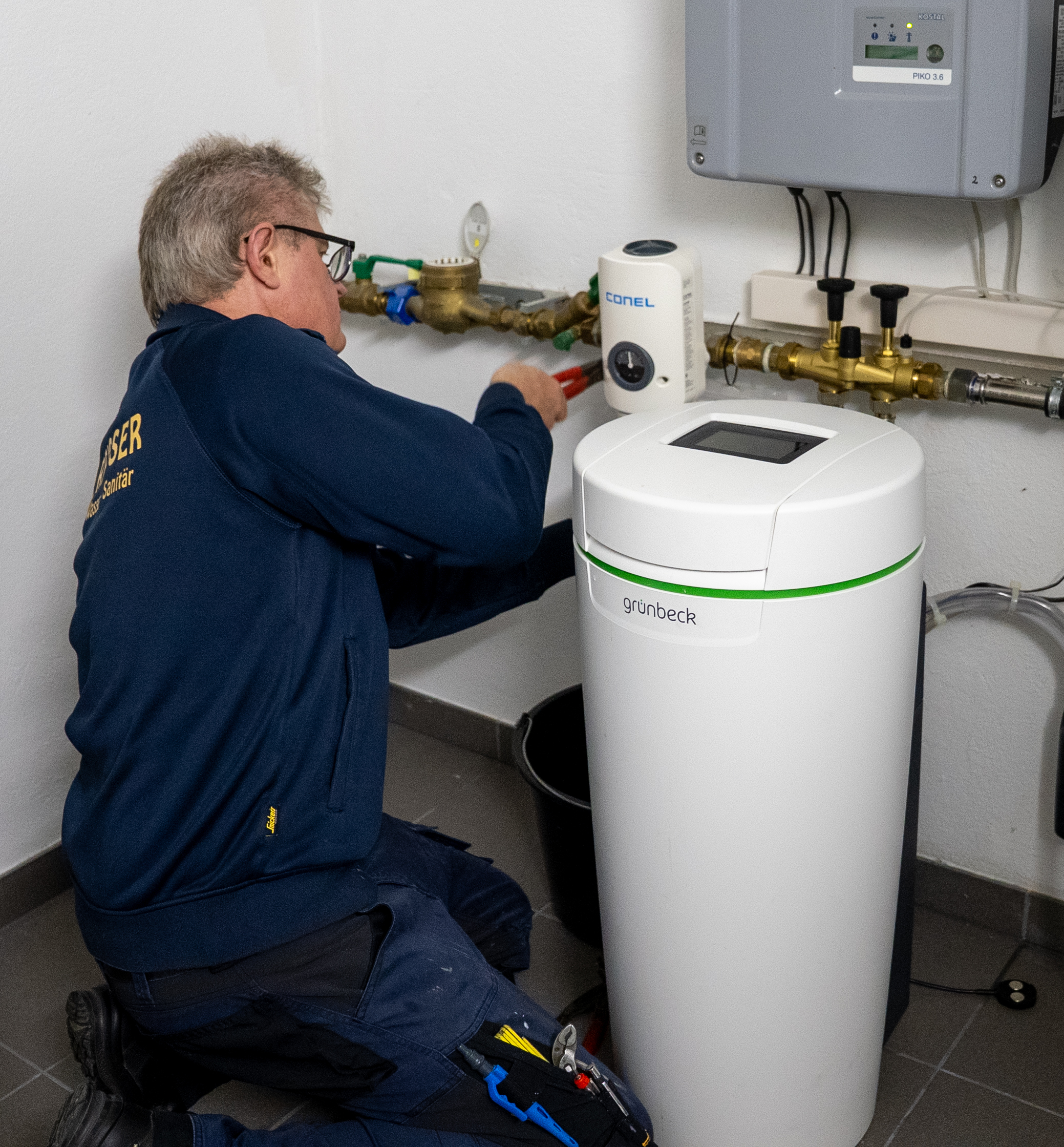 Handwerker repariert Wasseraufbereitungsanlage der Marke Grünbeck an Rohrleitung in Hauswirtschaftsraum.
