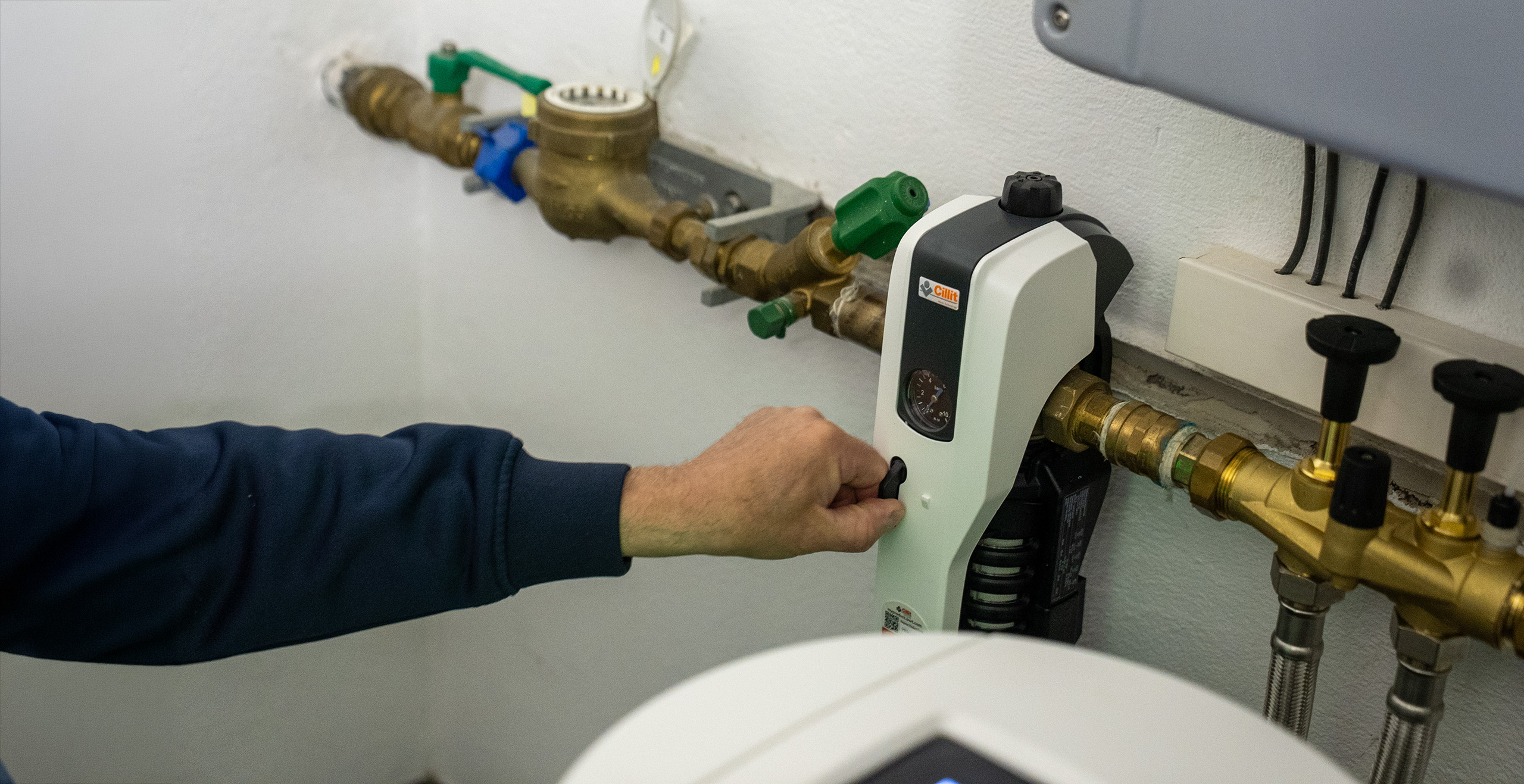 Hand adjusts a control on a white heating or water system device with copper pipes attached.