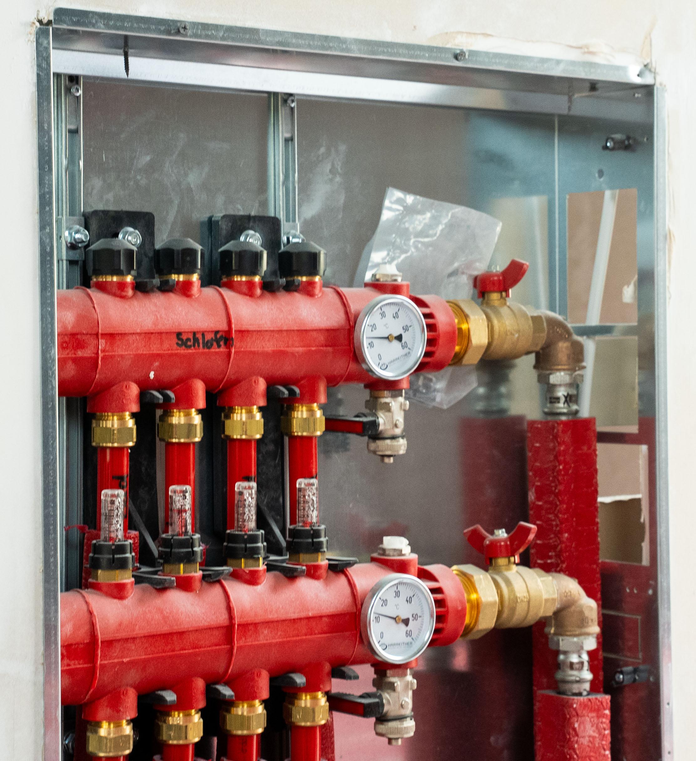 Rotes Heizverteilerrohr mit Druck- und Temperaturanzeigern in einem Metallkasten an der Wand.