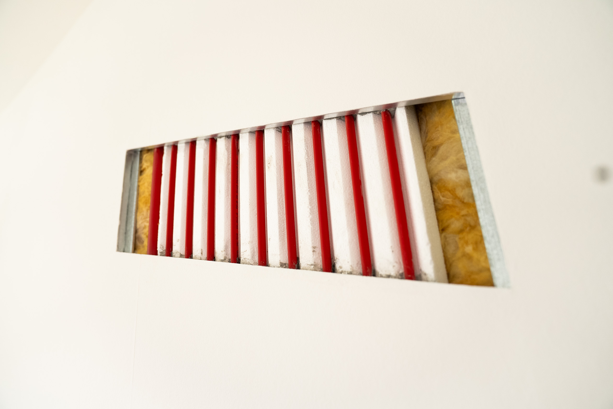 In eine Wand eingelassene Heizungsrohre mit roter Isolierung und gelber Dämmung innen