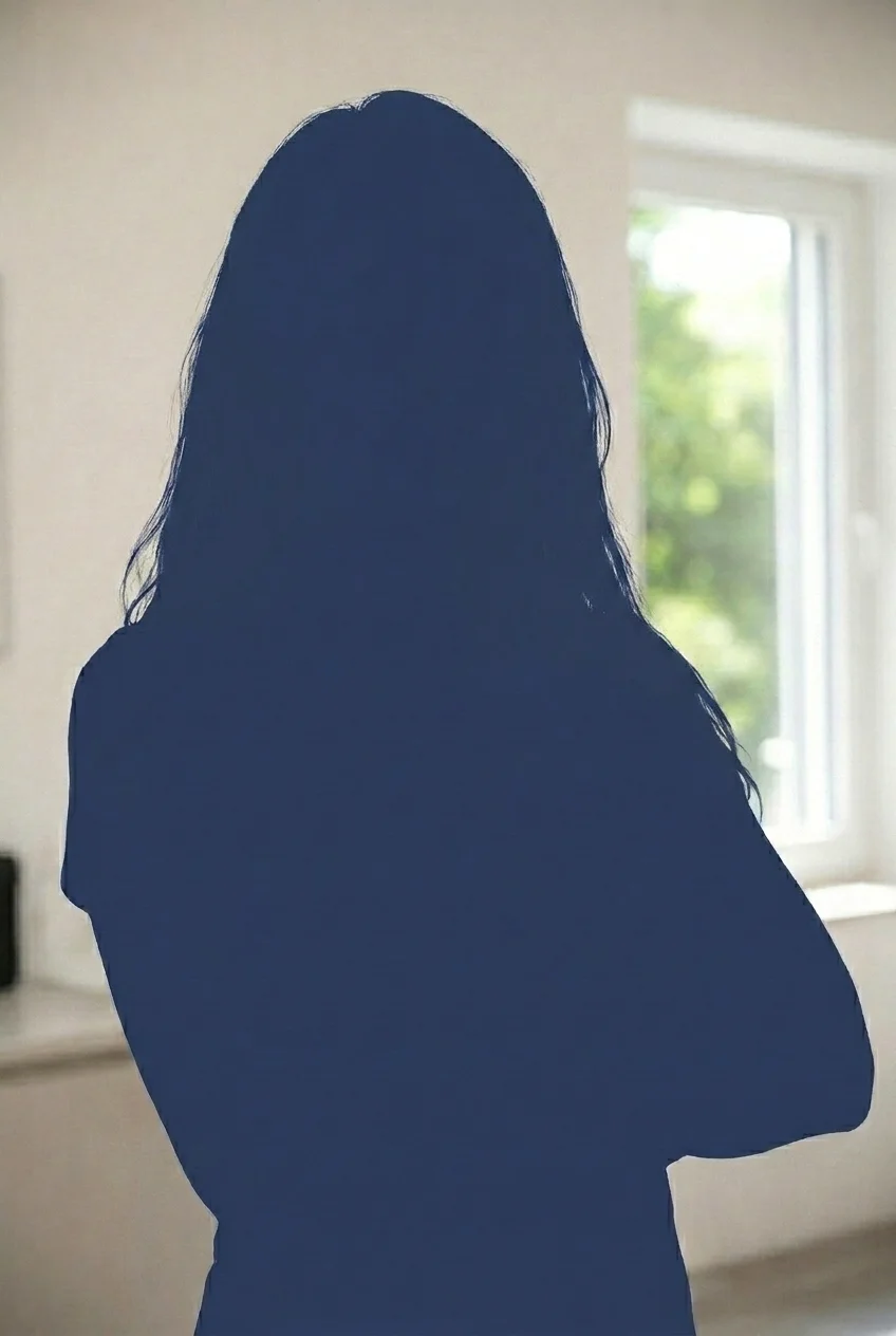 Silhouette einer Frau mit langen Haaren, die vor einem Fenster mit Blick ins Grüne steht.