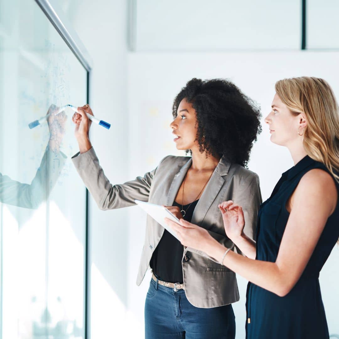 Two colleagues mapping a structure on a glass wall, working through a brand architecture exercise.