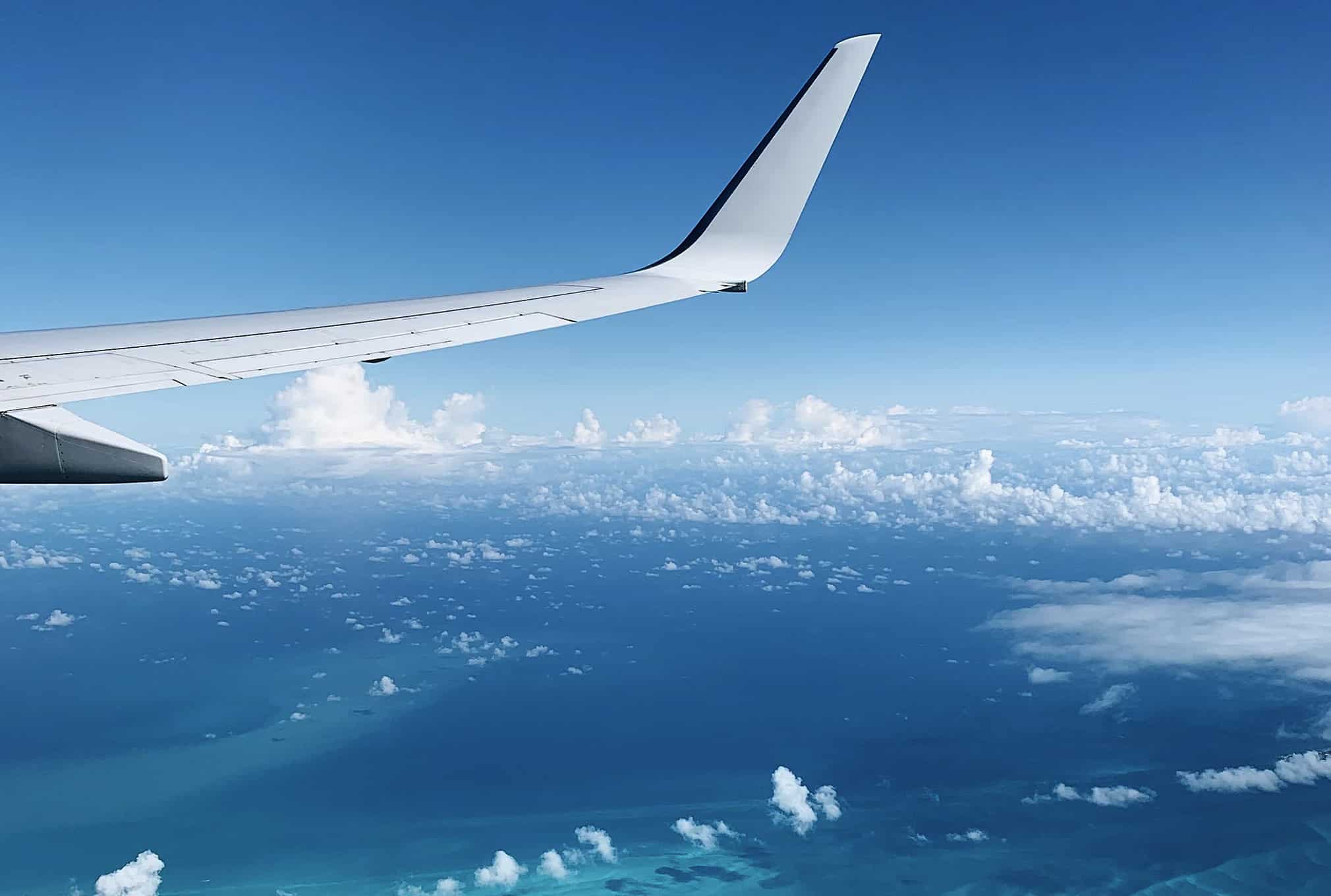 An aircraft wing seen from the cabin window above cloud and open sea.