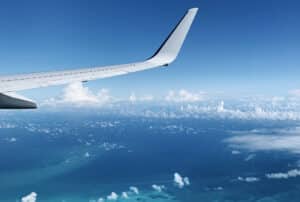 An aircraft wing seen from the cabin window above cloud and open sea.