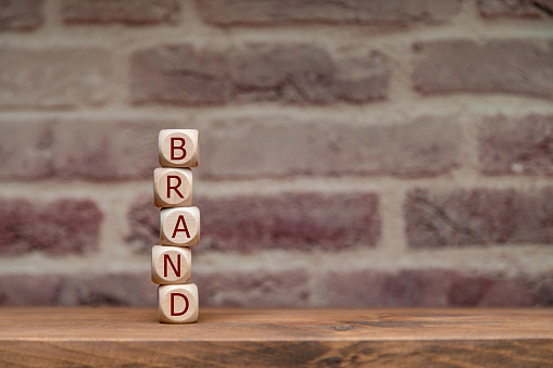 Wooden blocks spelling BRAND stacked vertically against an exposed brick wall.