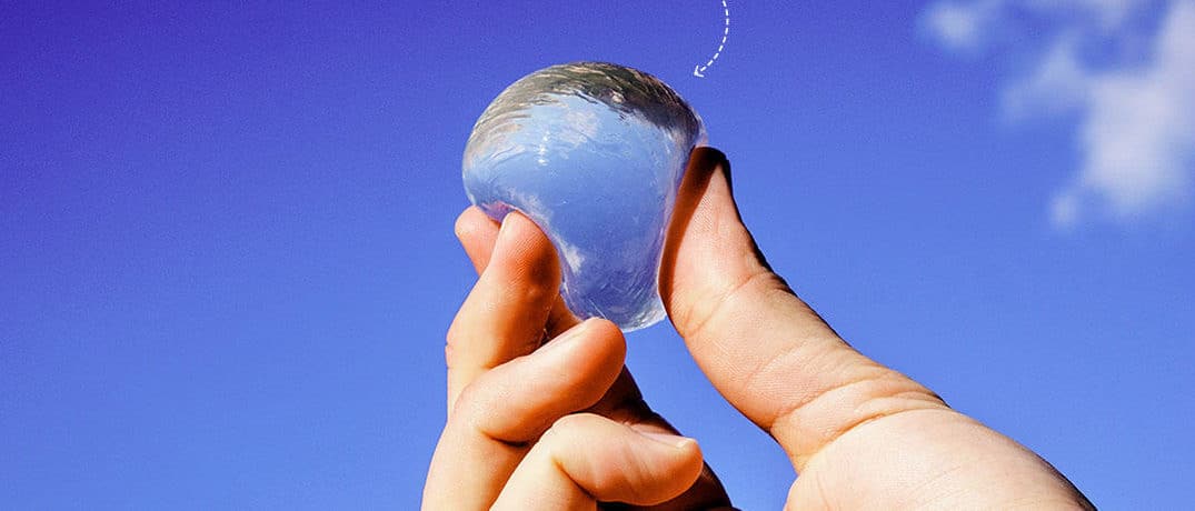 A hand holding an Ooho edible water pouch, the seaweed-based alternative to a plastic bottle.
