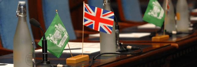 Saudi and British flags on a conference table with microphones, set for an Arab-British Chamber of Commerce meeting.