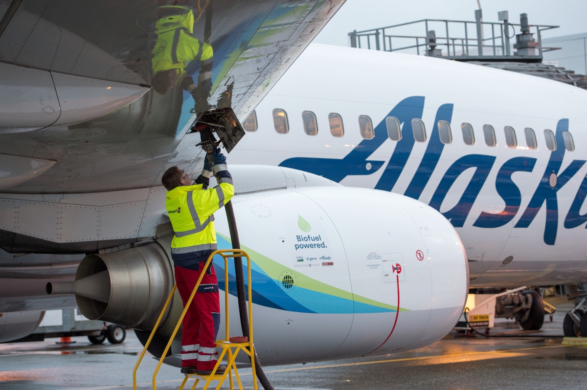 Ground crew refuelling an Alaska Airlines aircraft marked Biofuel powered, beside the airline's Eskimo tail livery.