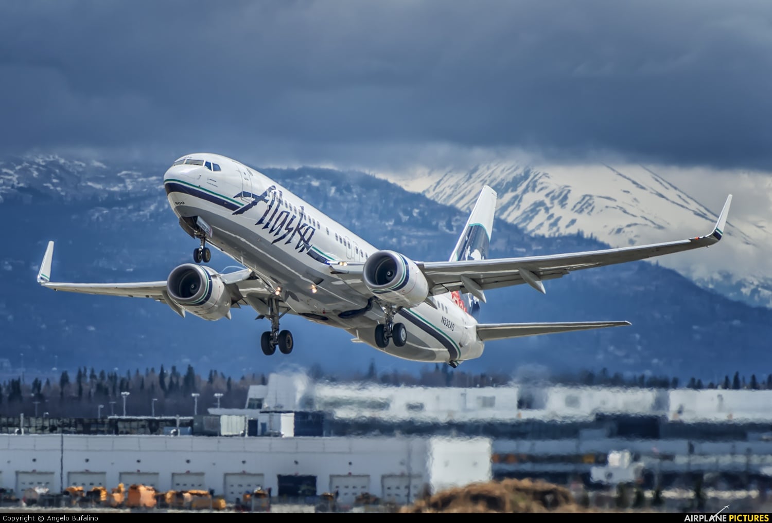 An Alaska Airlines aircraft taking off with snow-covered mountains behind.