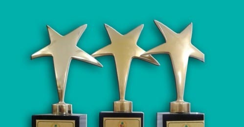 Three gold star-shaped trophies on a turquoise background, the awards won by flynas.