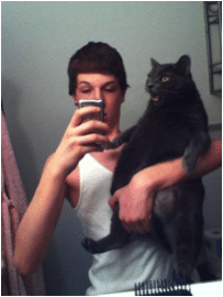 A man taking a mirror selfie while holding a black cat.