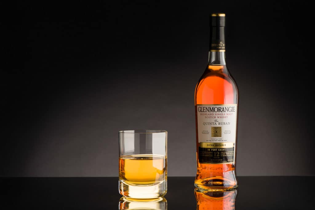 A bottle of Glenmorangie Quinta Ruban whisky beside a filled tumbler on a dark background.
