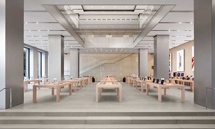 The interior of a flagship Apple Store, with product display tables lit under a high stone-and-glass retail space.