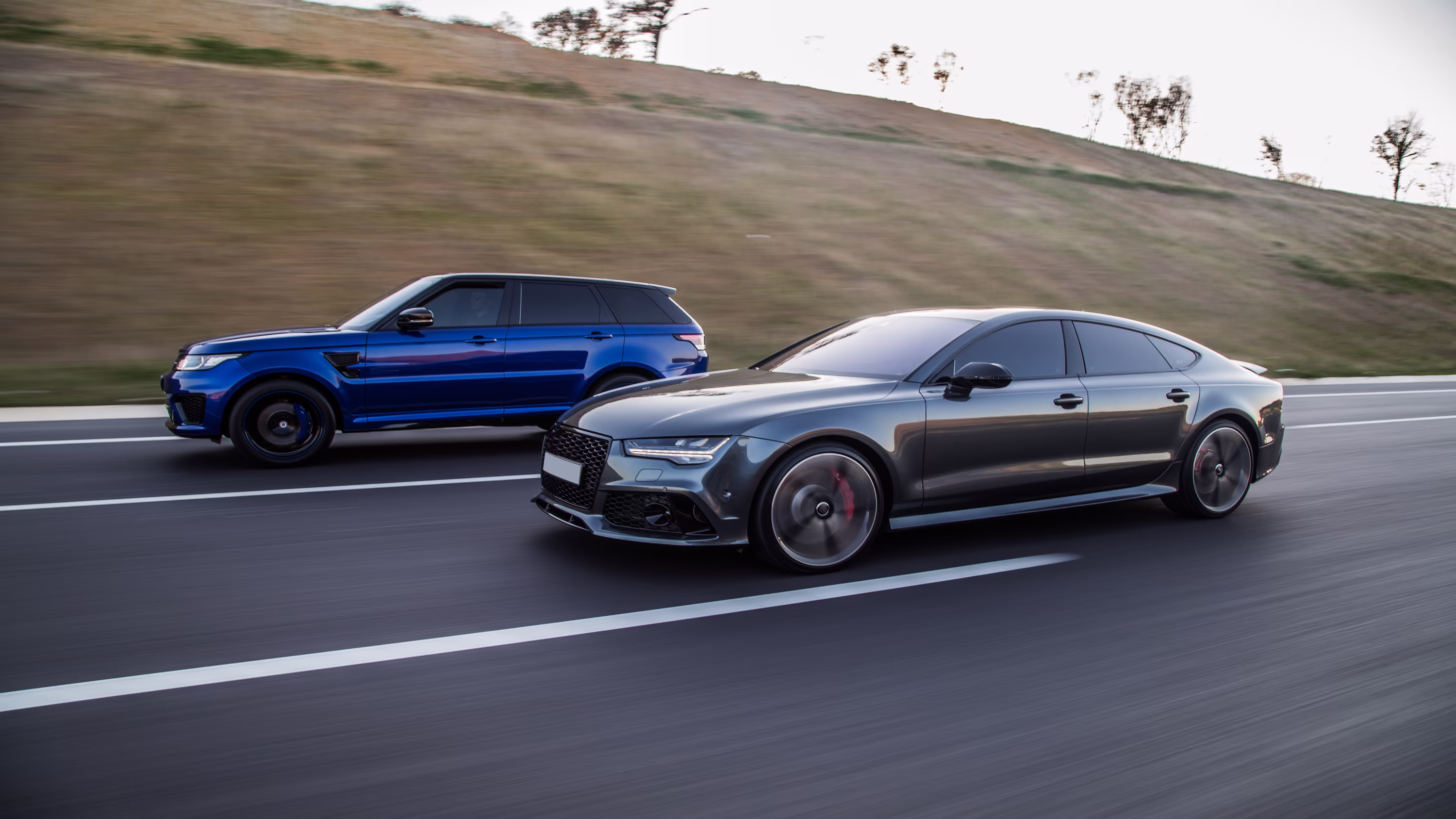 A blue SUV and a grey saloon driving side by side along an open road | Automotive