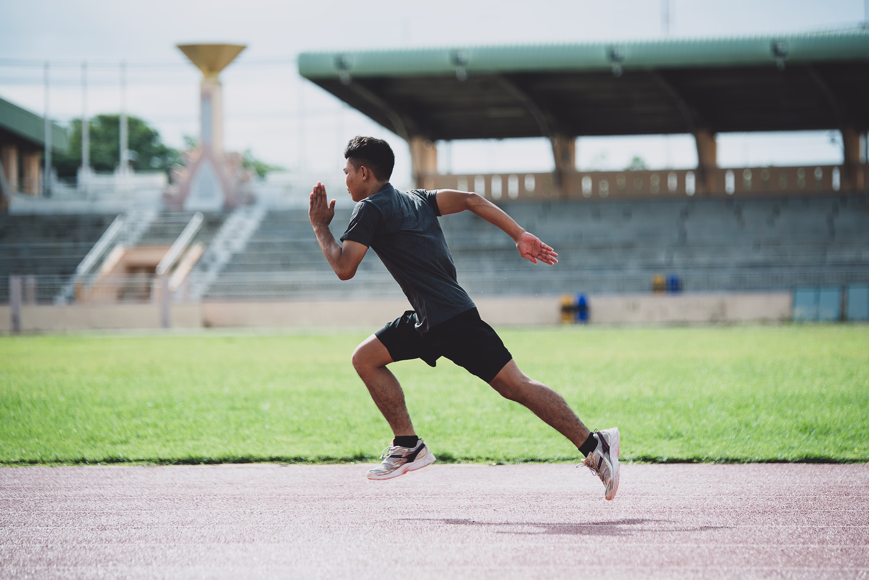 A sprinter accelerating along a running track in front of empty stadium seating | Sports