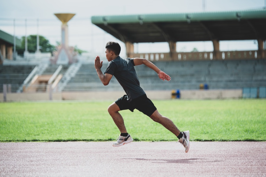 A sprinter accelerating along a running track in front of empty stadium seating | Sports