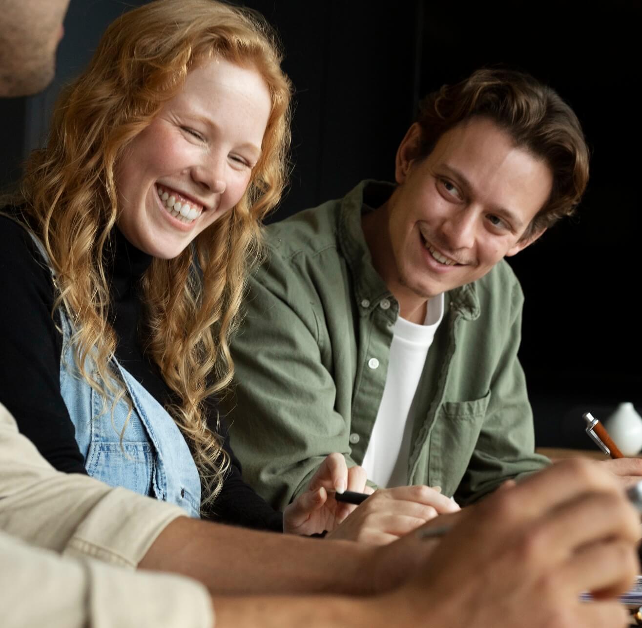 Two colleagues laughing together over notes at a shared desk | Brand Culture