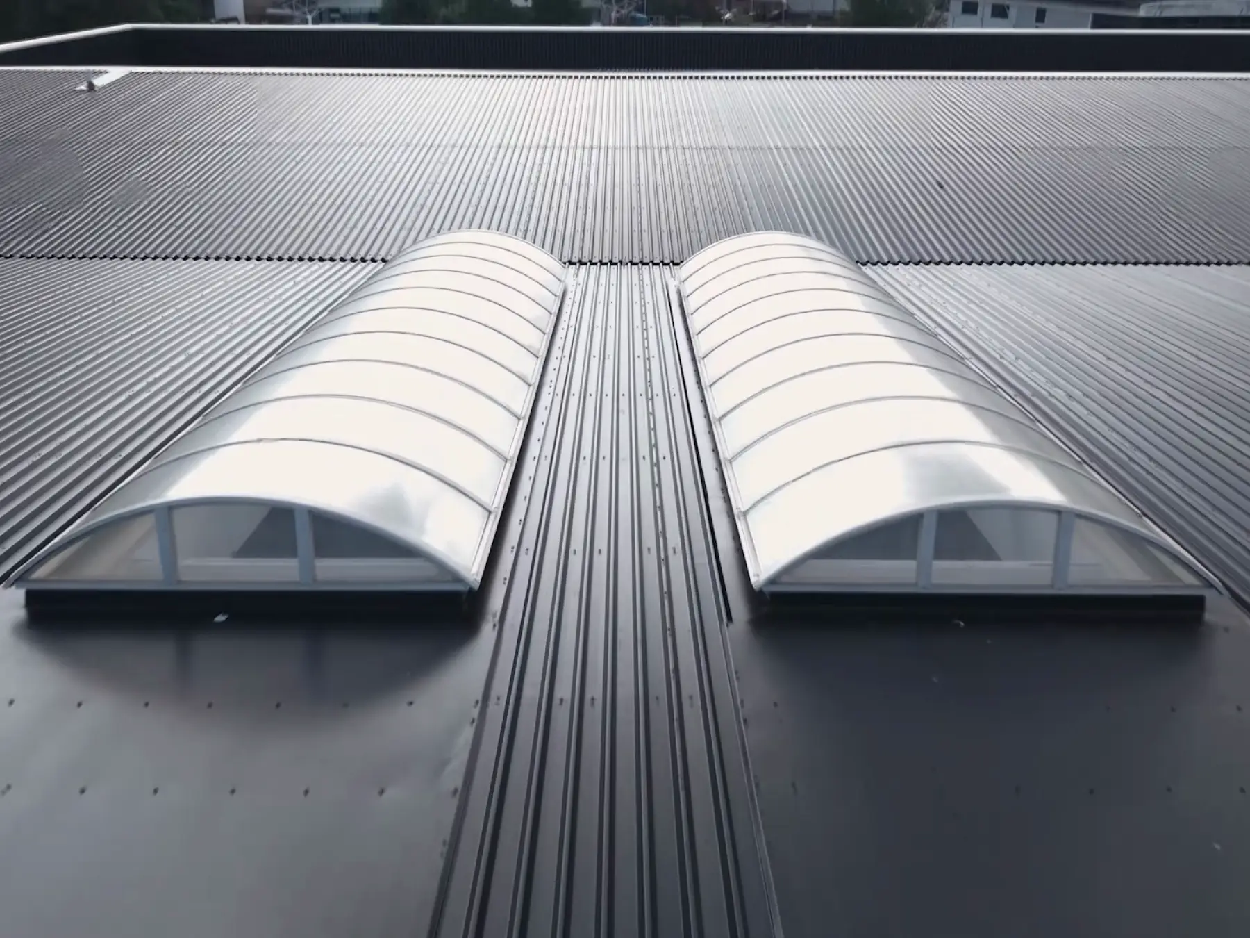 Close-up of two white curved rooflights installed side by side on a dark gray corrugated metal roof.