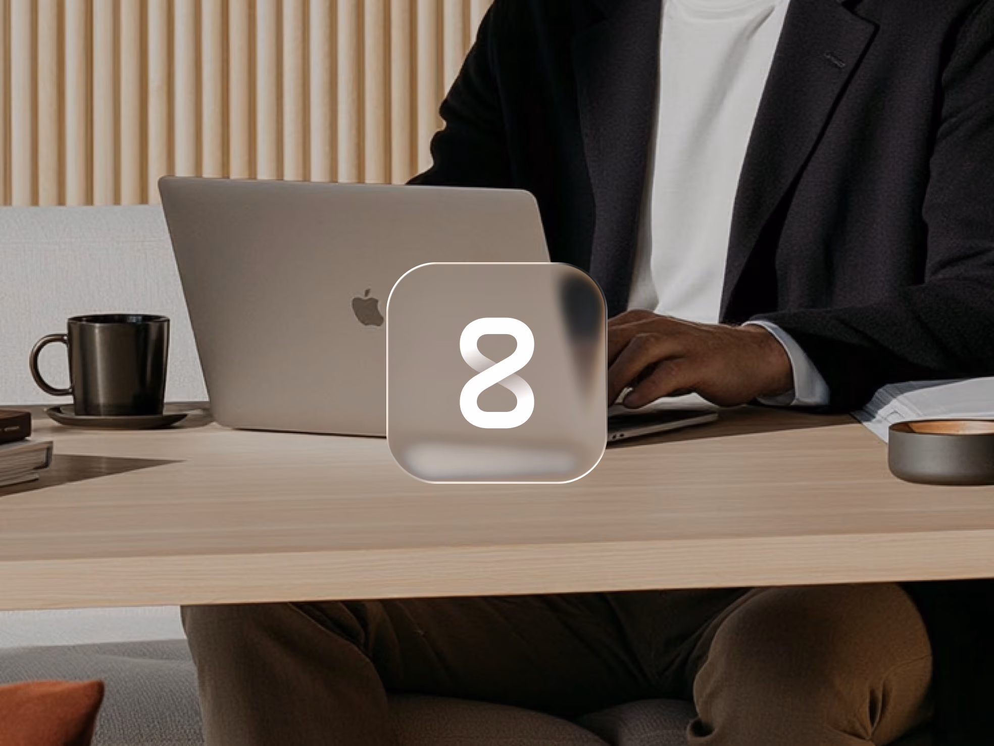 Person typing on a MacBook laptop at a wooden desk with a black coffee cup nearby.
