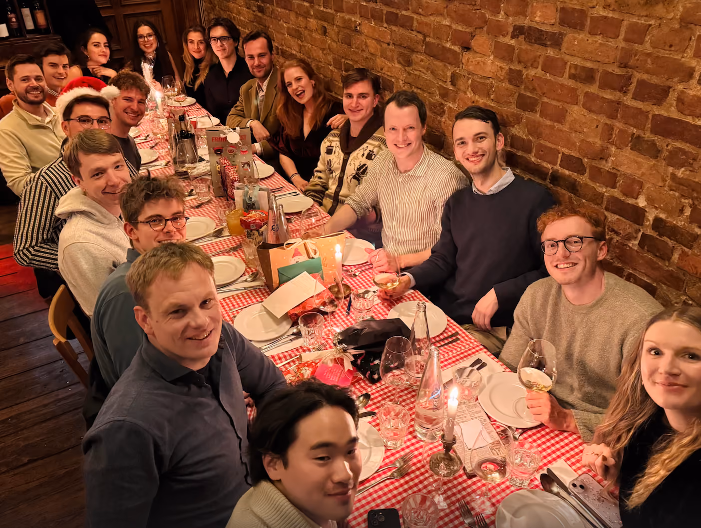 Group of people sitting around a checkered table with drinks and gifts, smiling at the camera.