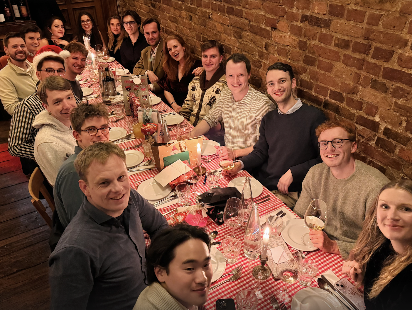 Group of people sitting around a checkered table with drinks and gifts, smiling at the camera.