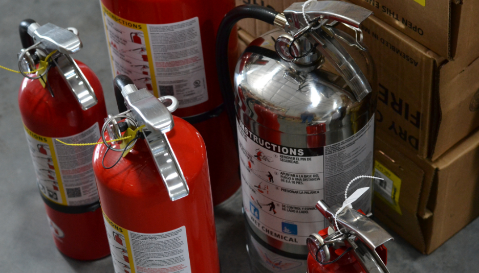 Red and silver fire extinguishers with safety pins on a gray floor near cardboard boxes.