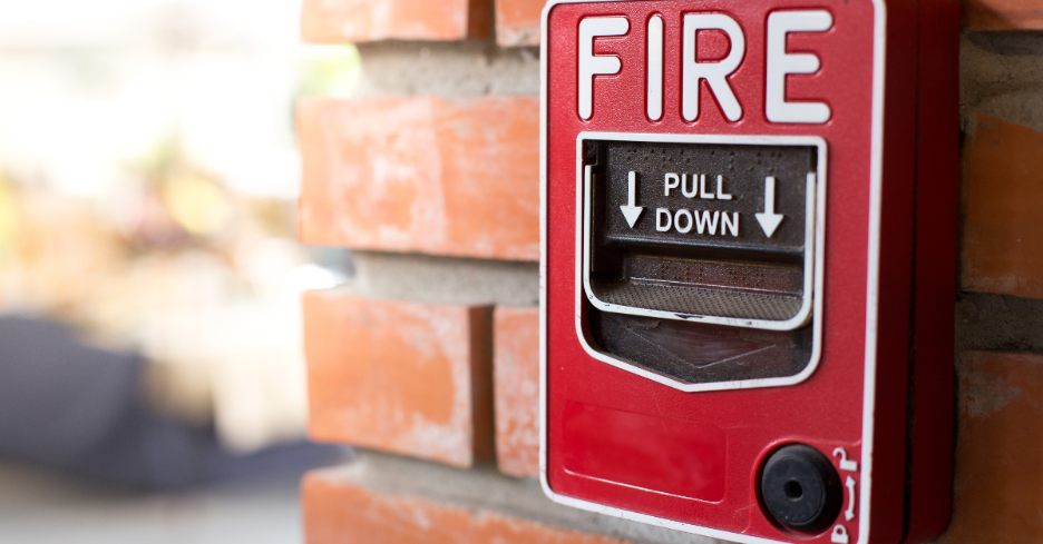 Close-up of a red fire alarm pull station mounted on a brick wall with 'FIRE PULL DOWN' text.