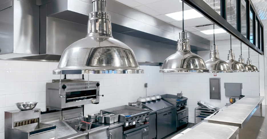 Modern commercial kitchen with stainless steel cooking appliances and hanging industrial lights.