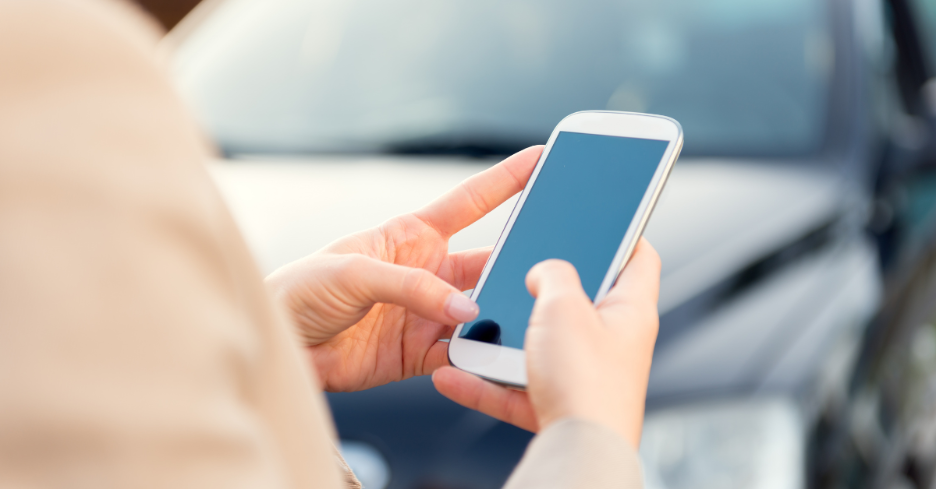 Person holding and interacting with a white smartphone with a black screen outdoors near a car.