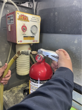 Person holding the handle of a red fire extinguisher near a hose and a GETZ machine.