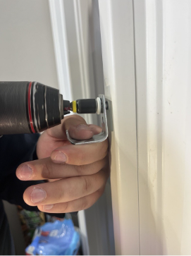 Person using a drill to screw a metal bracket onto a white door frame.