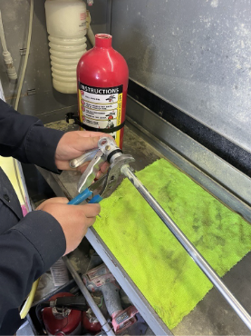 Hands holding a hose fitting near a red fire extinguisher on a green cloth-covered surface.