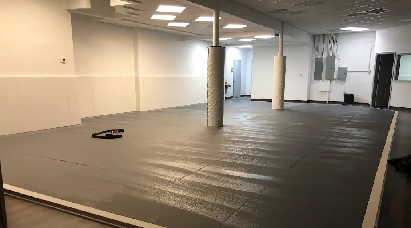 A spacious martial arts training area with padded mats, wall padding, and support columns inside a jiu jitsu academy.