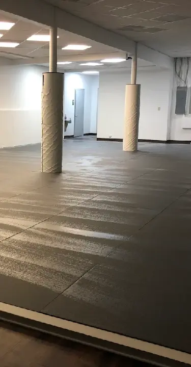 A spacious martial arts training area with padded mats, wall padding, and support columns inside a jiu jitsu academy.