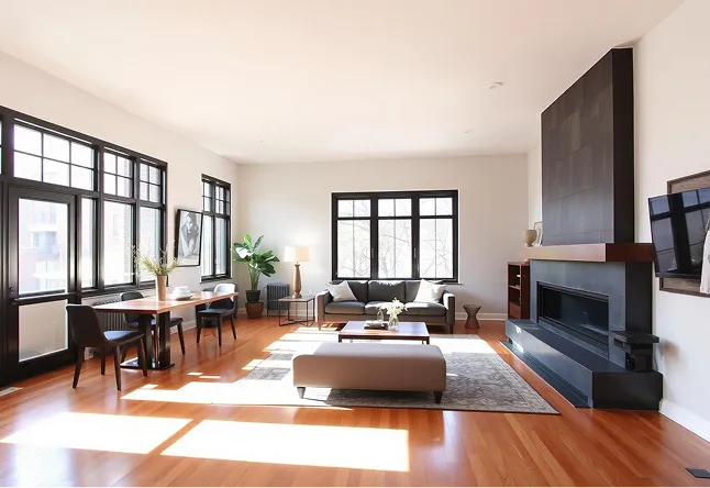 Bright modern living room with hardwood floors, gray sofa, black fireplace, and large windows.