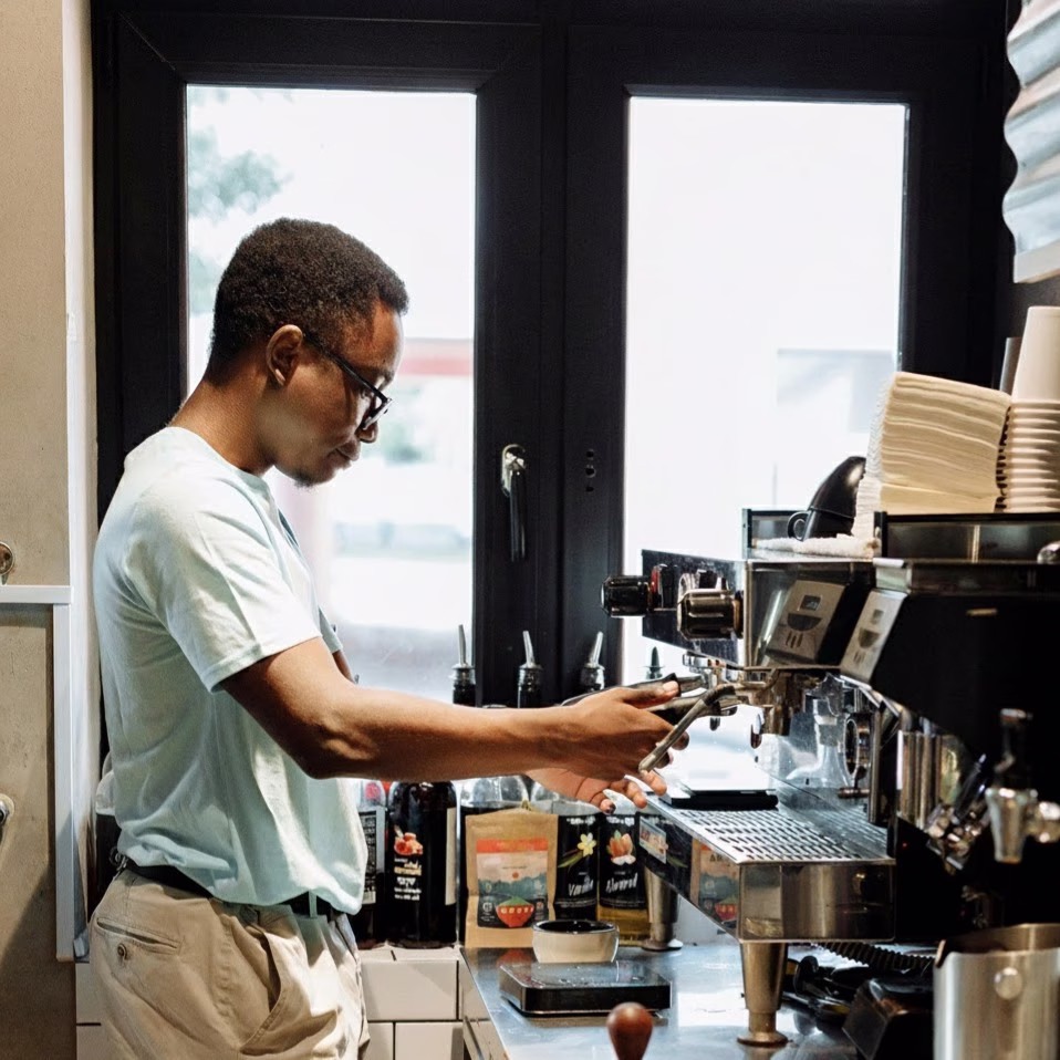 Barista attaching a portafilter to an espresso machine at a coffee shop counter.