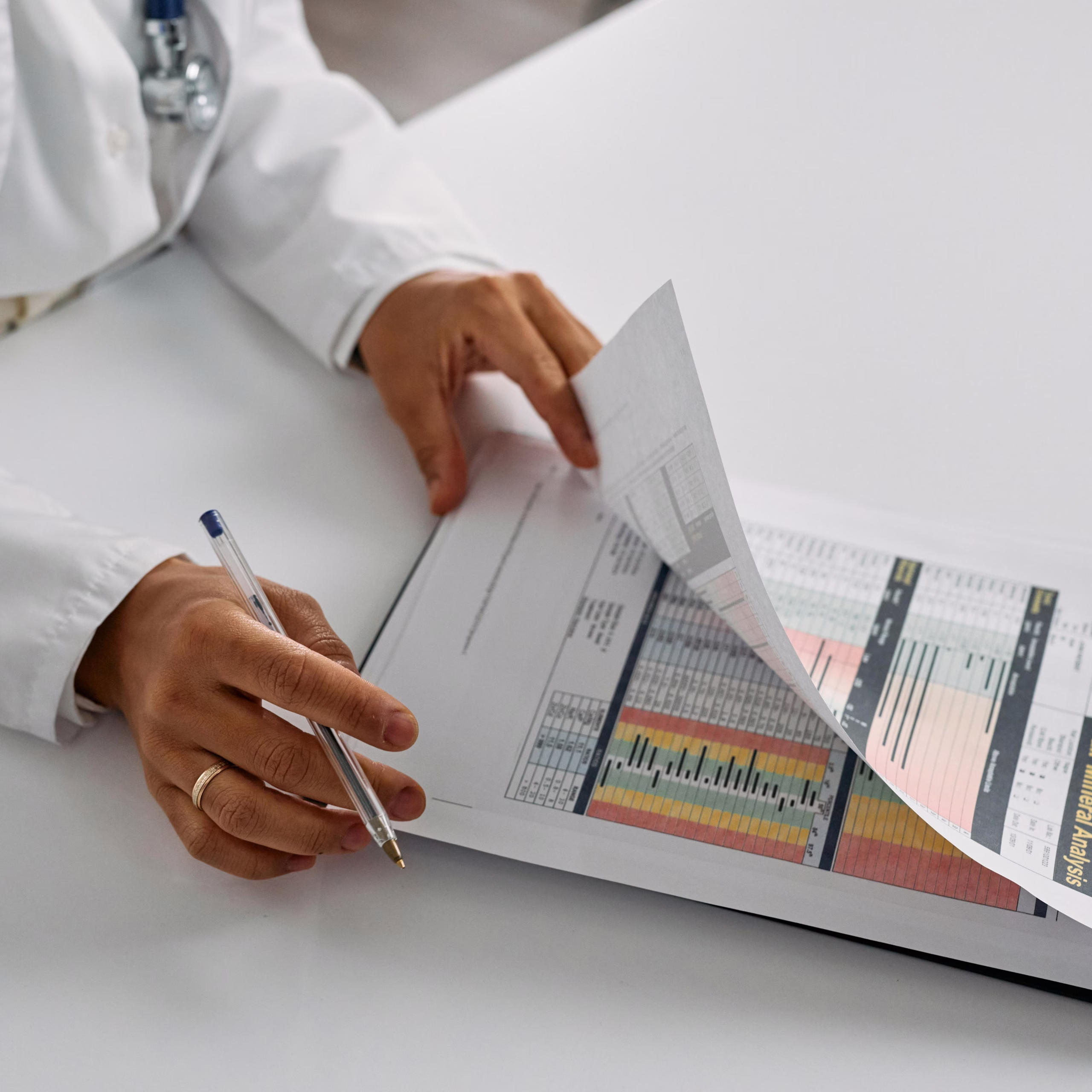 Doctor in a white coat holding a pen while reviewing a mineral analysis report with colored chart data.