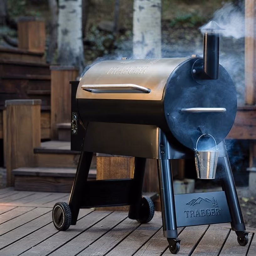 Traeger wood pellet grill with smoke rising from the chimney, on a wooden deck.